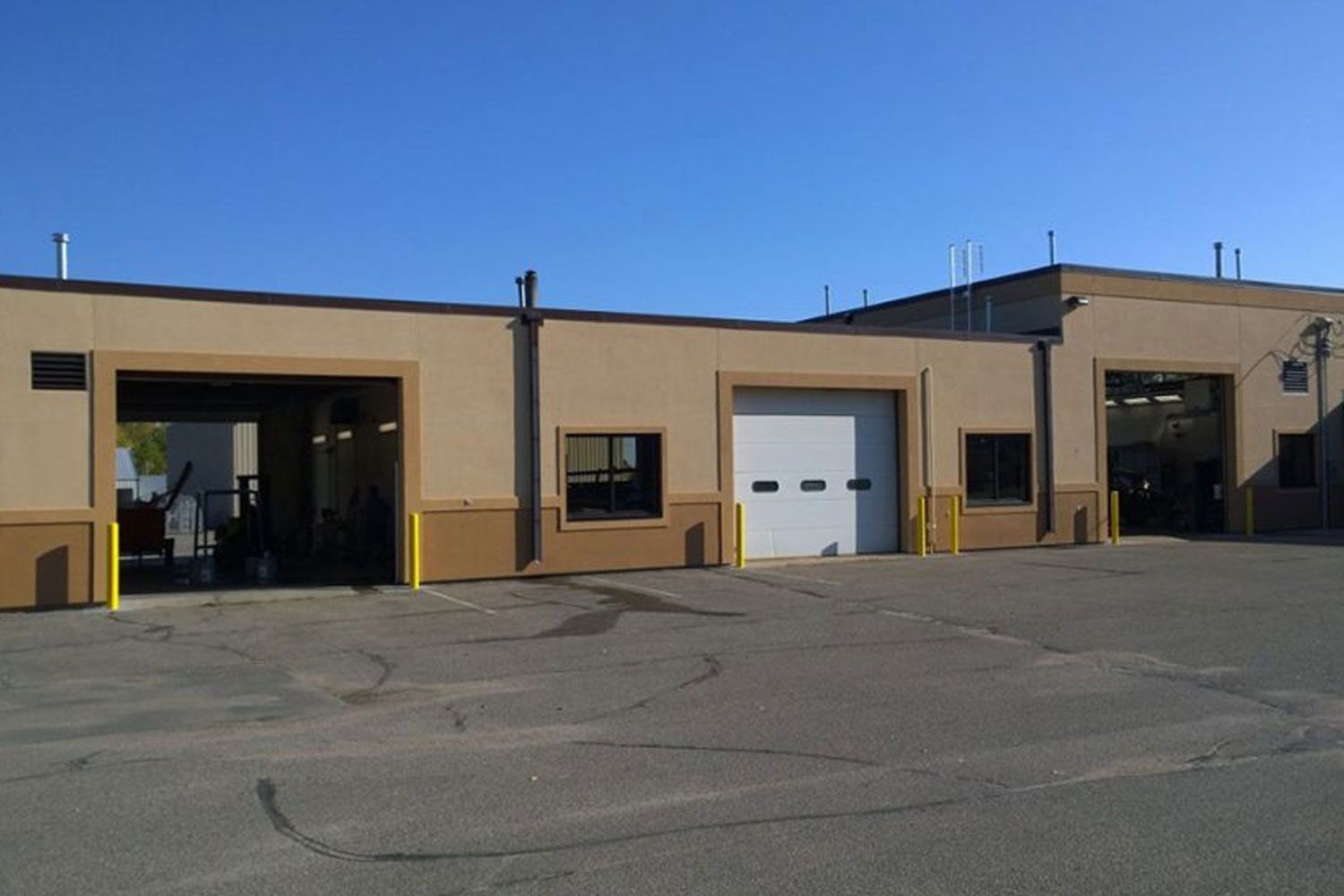 Exterior of a beige auto repair shop with three garage doors. Clear blue sky overhead.