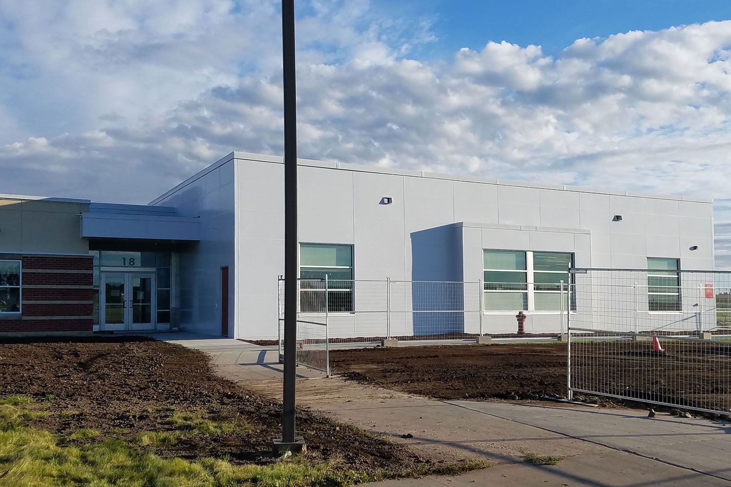 Exterior view of a light gray building with windows, front entrance, and temporary fencing in front.