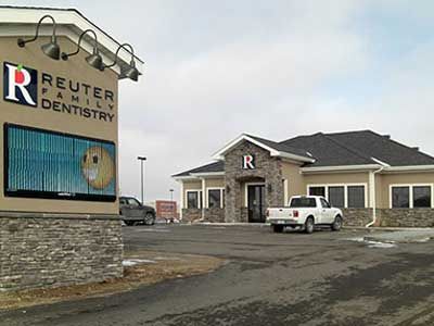 Reuter Family Dentistry building with sign; white truck parked in front. Beige building, blue sky.