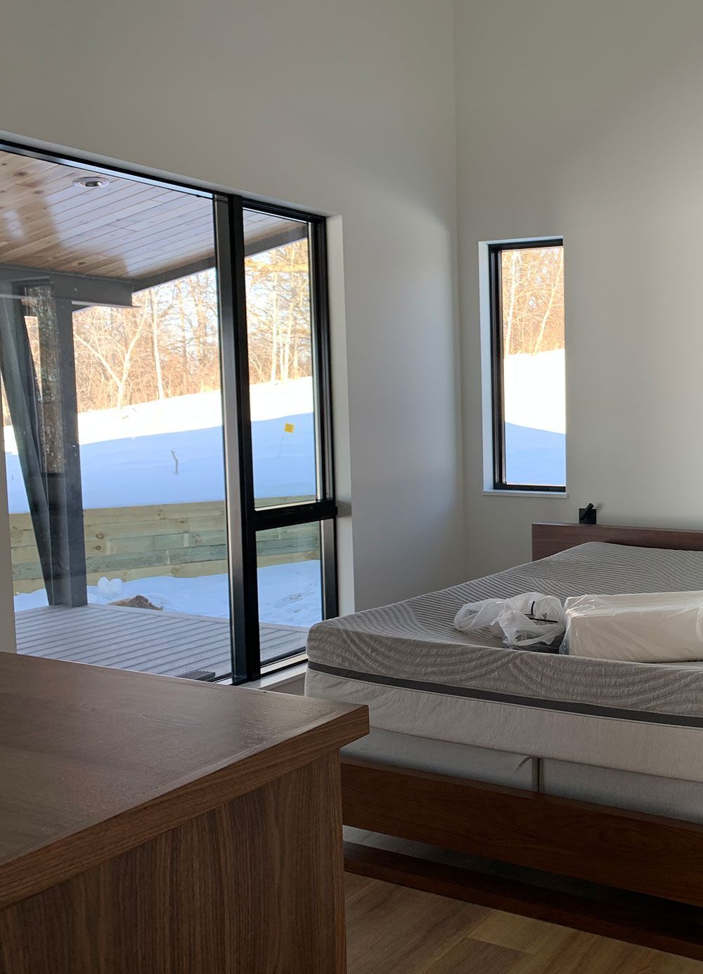 Bedroom with bed, large window overlooking snowy landscape, and small side window.