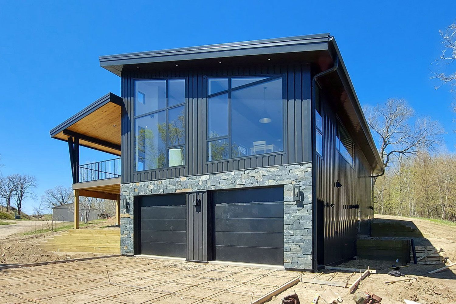 Modern two-story building with black garage doors and floor-to-ceiling windows; gray stone accents. Blue sky background.
