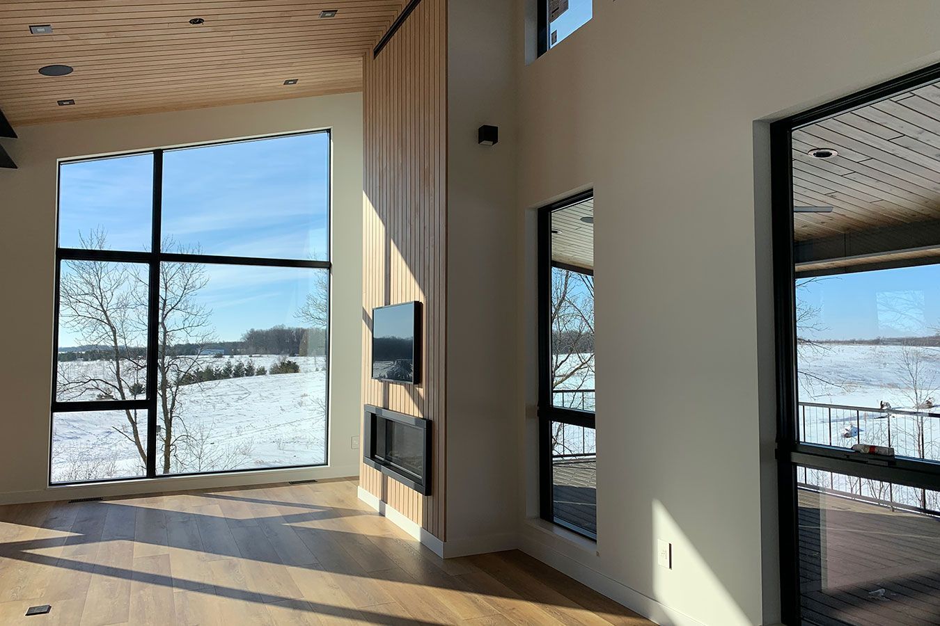 Spacious room with large windows overlooking a snowy landscape, natural wood accents, and a fireplace.