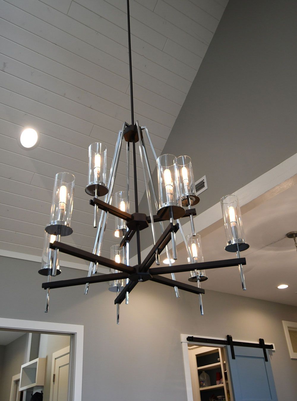 Dark bronze chandelier with glass shades hanging from a white, sloped ceiling.