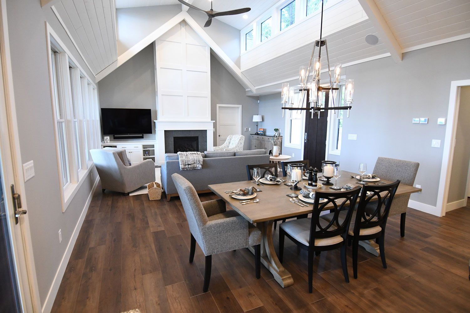 Open-concept living space with dining area and fireplace. Gray walls, wood floor, and chandelier.