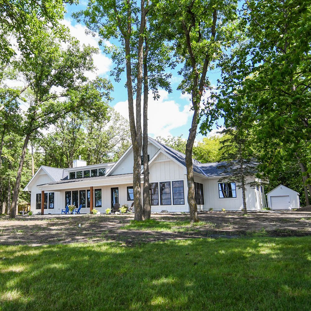 White modern home with large windows, surrounded by trees and a garage.
