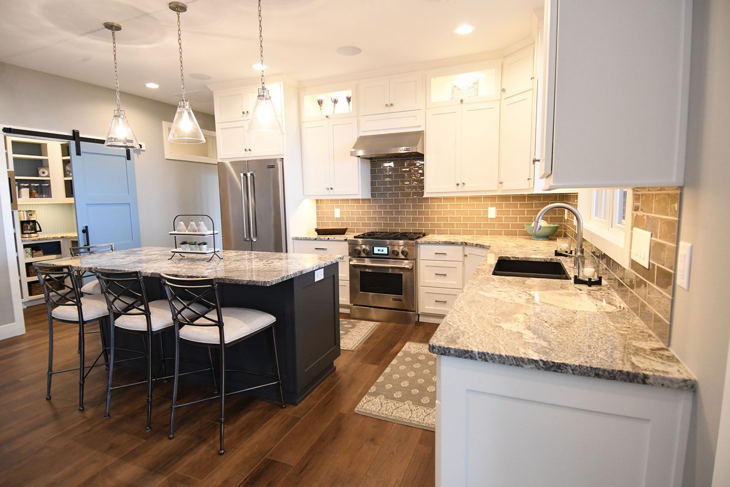 Modern kitchen with white cabinets, granite countertops, island with seating, and stainless steel appliances.