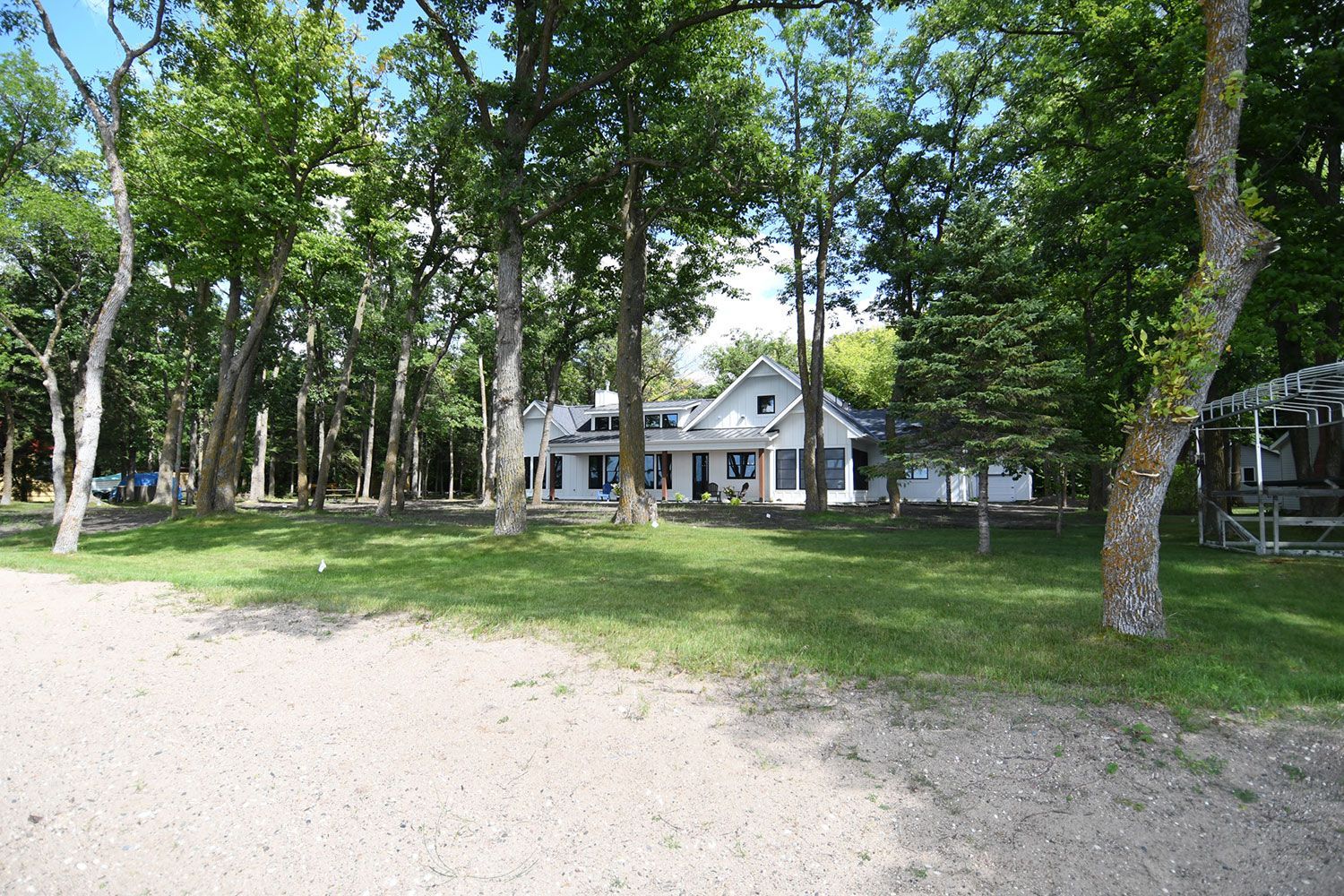 White house nestled among trees near sandy shore.