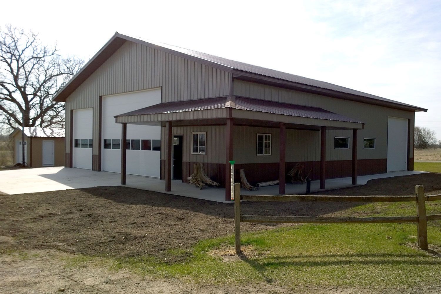 Large metal building with garage doors and a covered porch, in a rural setting.