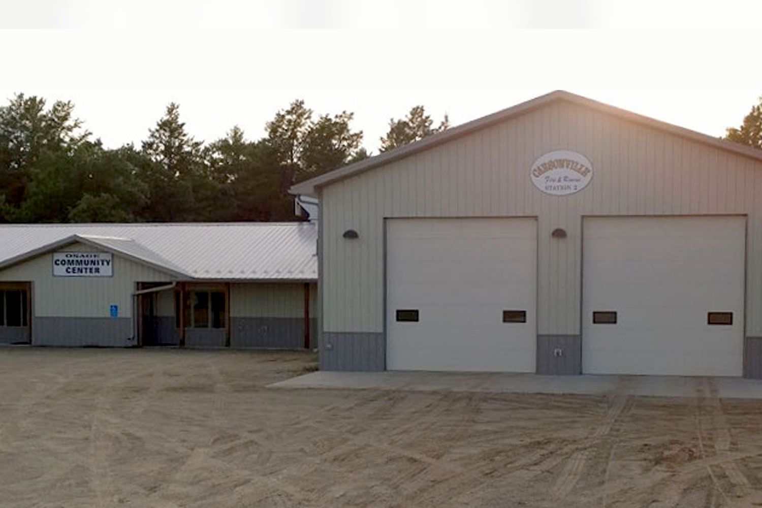 Light gray building with two garage doors, sign, and adjoining office; outdoor setting.