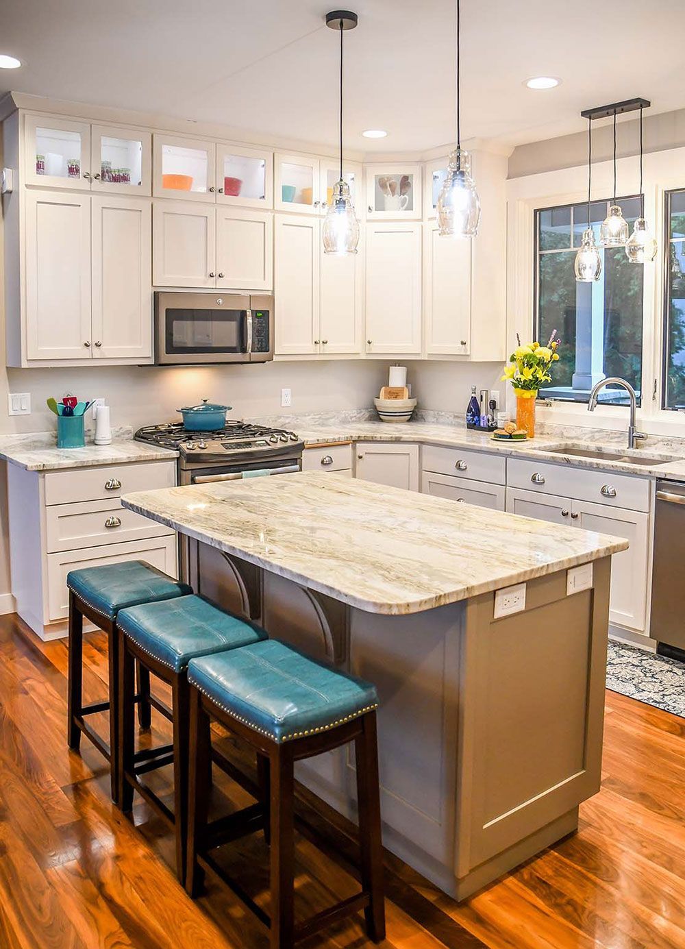 Kitchen with light-colored cabinets, granite countertops, an island with teal stools, and hardwood floors.