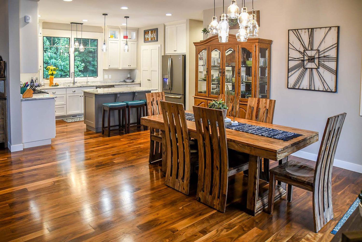Open kitchen and dining room with wood table and chairs. Dark wood floor. White cabinets and gray island.