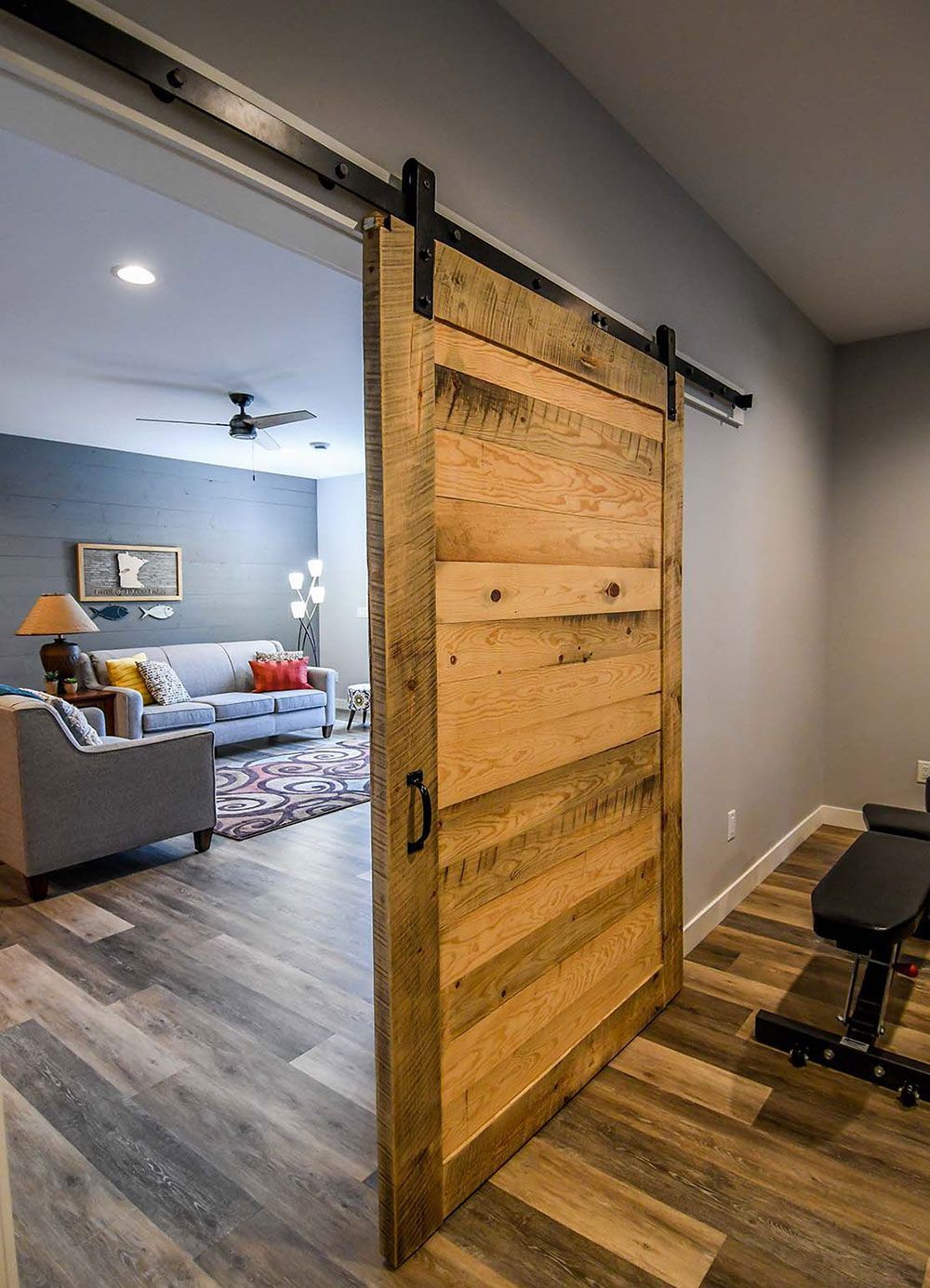 Barn door opens to living area with couch and a weight bench, wood door and floor.