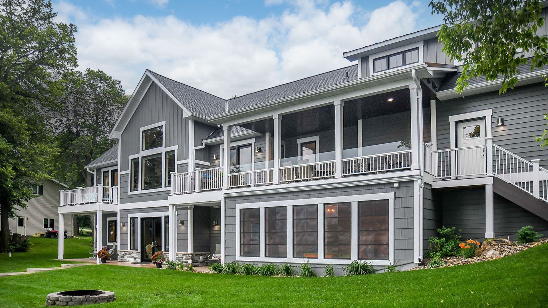 Gray two-story house with large windows, a porch, and green lawn under a blue sky.