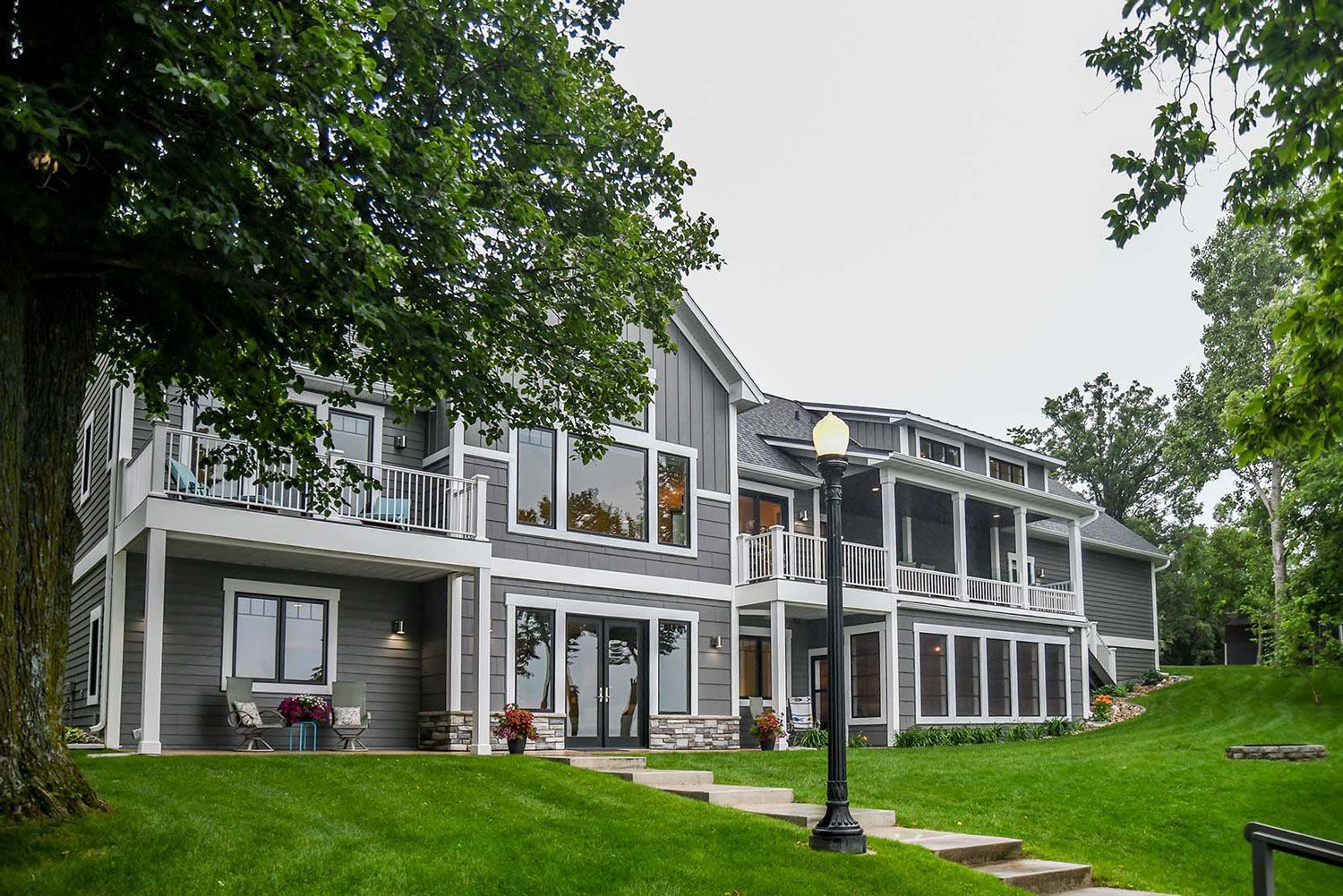 Gray house with white trim, balconies, and a lamp post on a grassy hill.