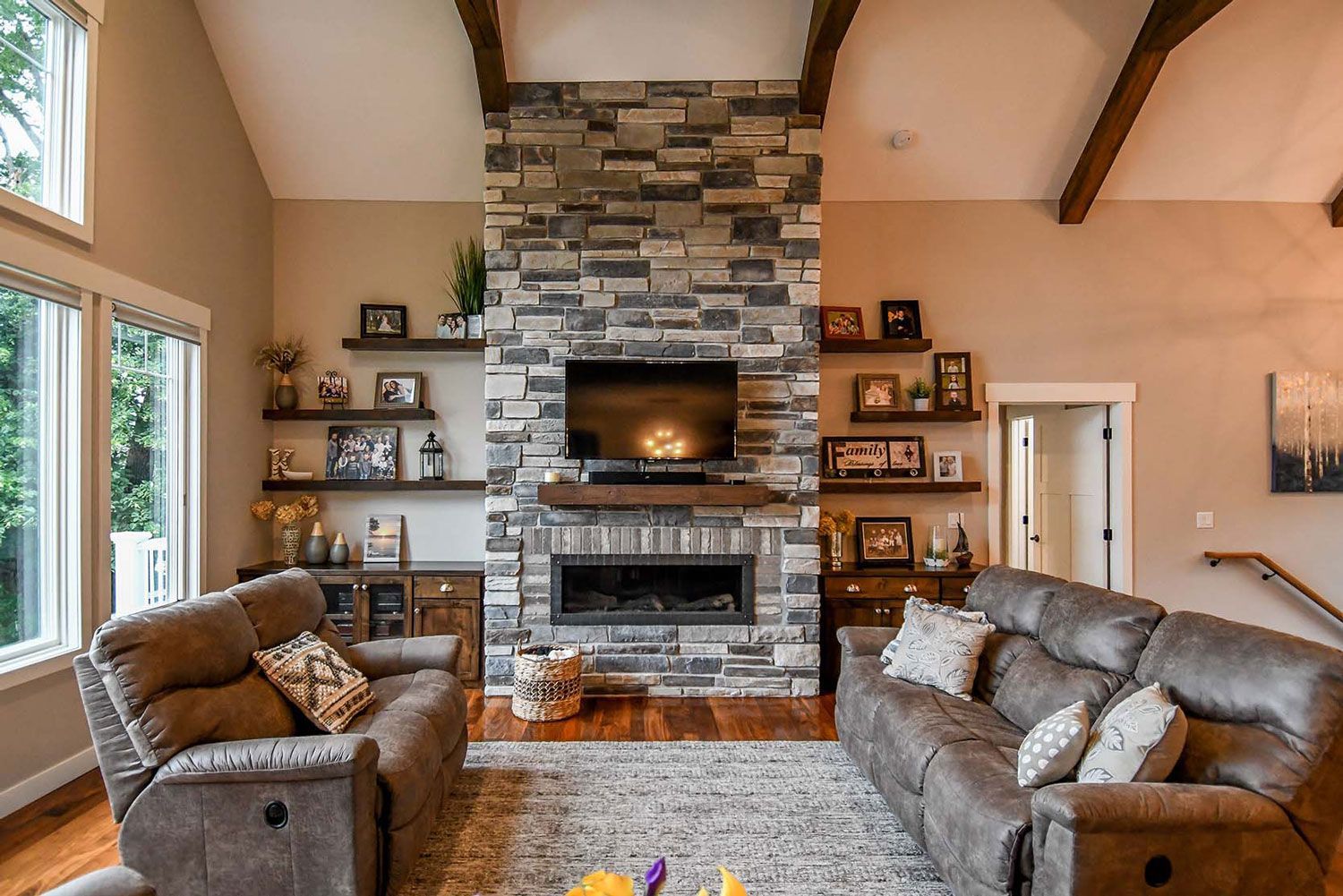 Living room with stone fireplace, TV, brown recliners, wood shelves with decor.