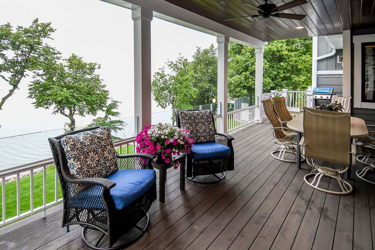 Covered porch with lake view, wicker chairs with blue cushions, and dining area.