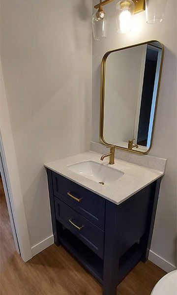Navy blue bathroom vanity with gold accents, white countertop, mirror, and light fixture.
