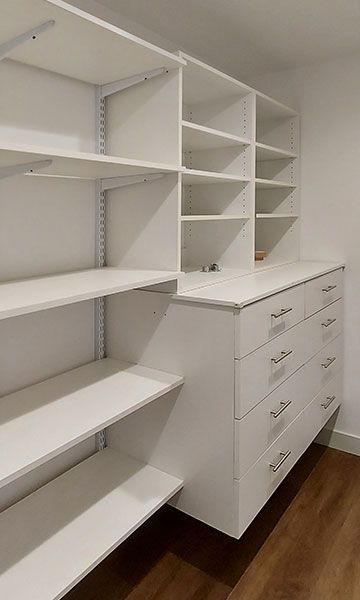 White closet shelving system with drawers and shelves in a room with wood floors.