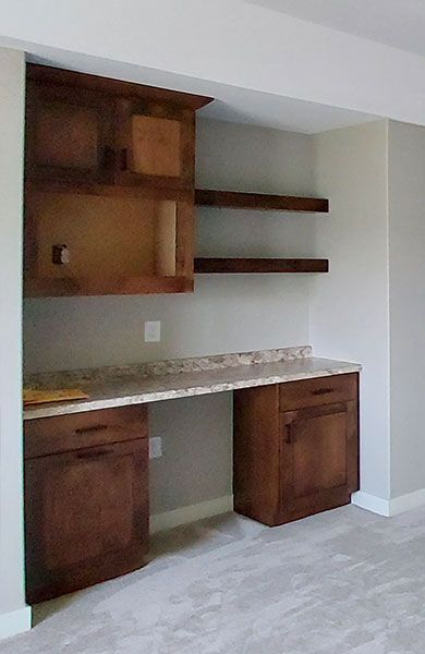 Built-in wooden desk with drawers and cabinets, beneath floating shelves. Neutral colors in a home setting.