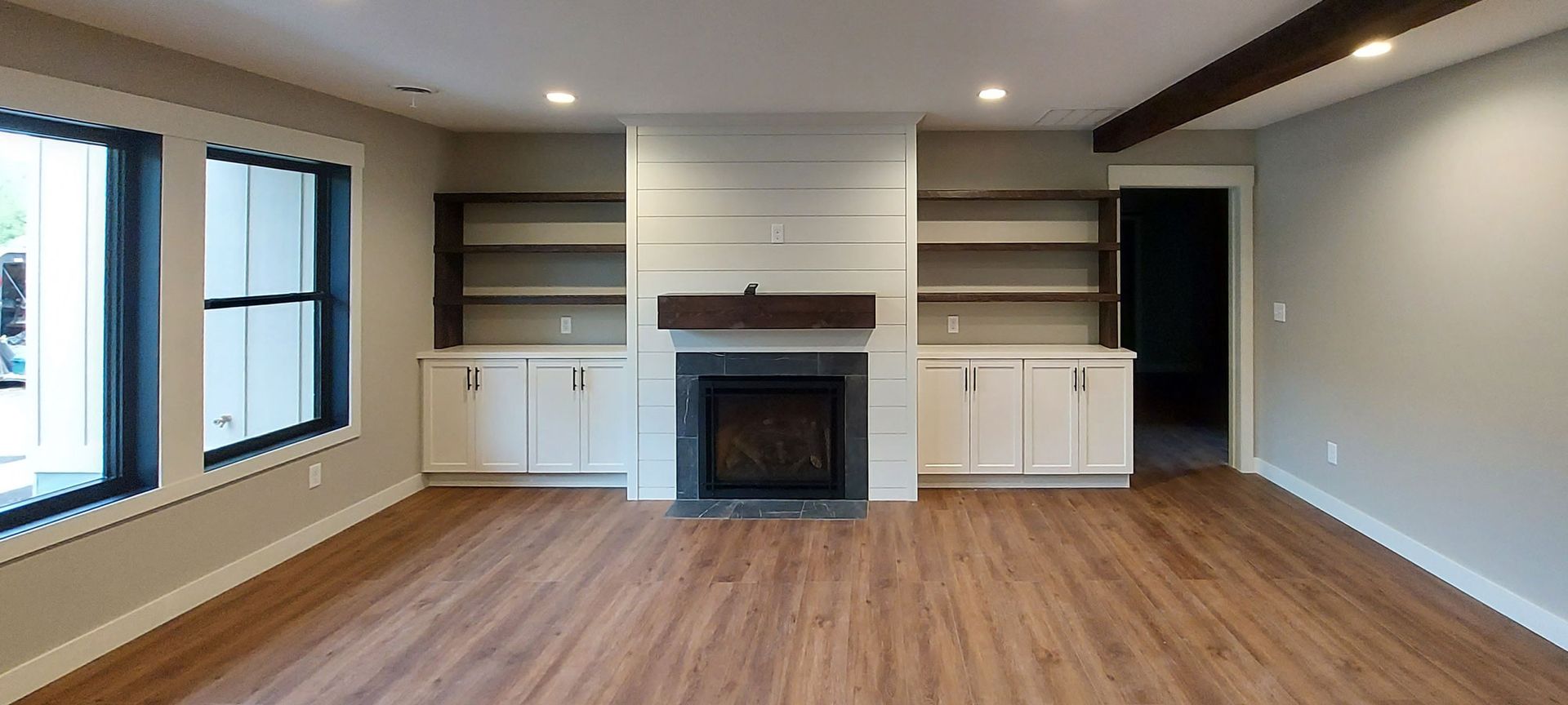 Living room with a fireplace, built-in shelves, white cabinets, and wood flooring.