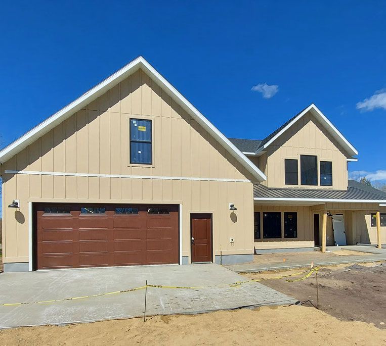 Tan house under construction with brown garage door and blue sky.