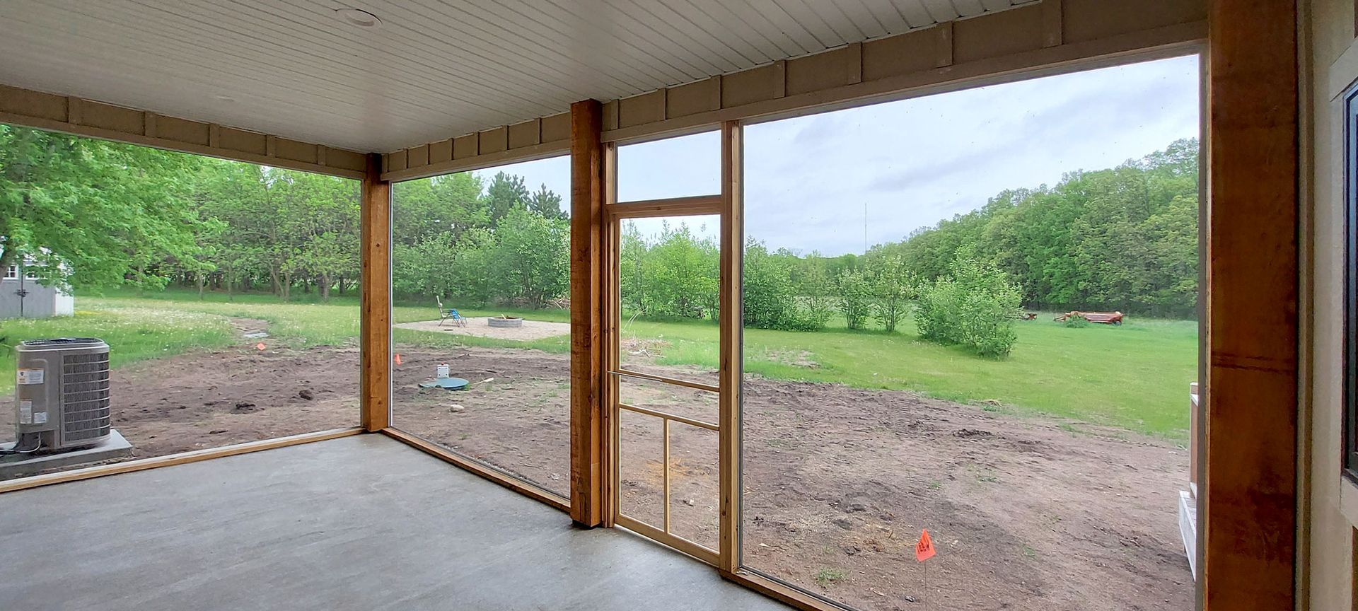 A screened-in porch overlooking a green field and trees under a cloudy sky.