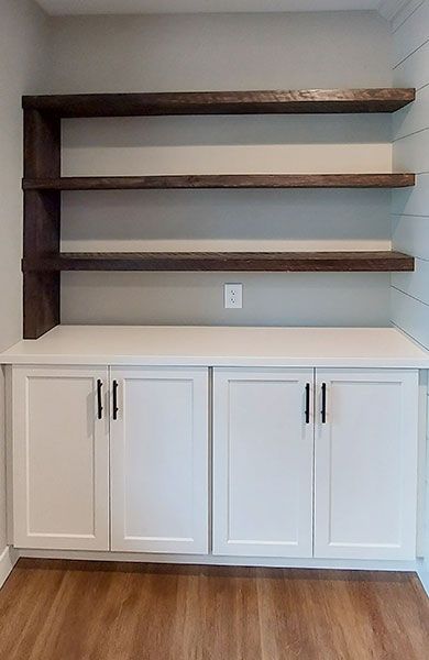 White cabinets with black handles and dark shelves against a neutral wall.