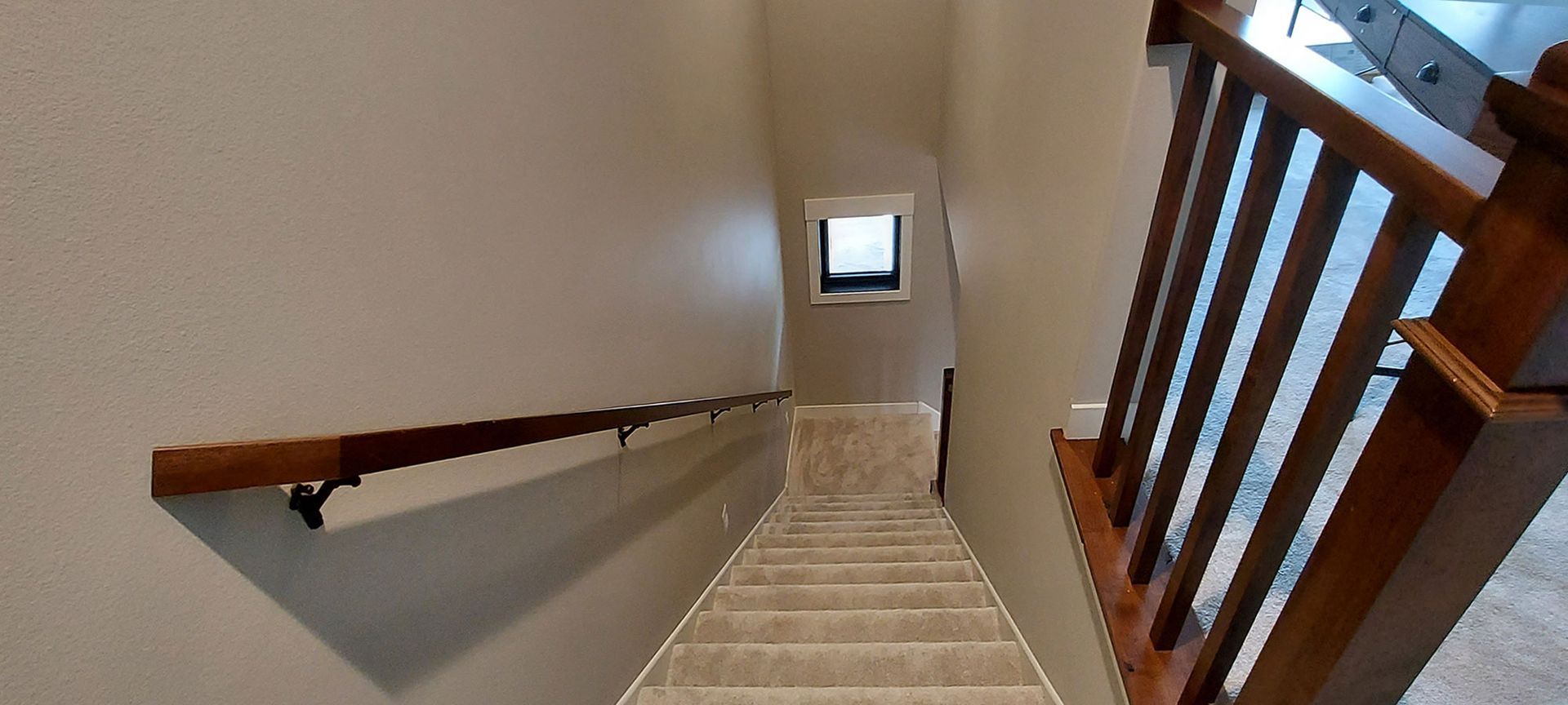 Staircase with wooden railing and handrail, leading downward toward a window at the end.