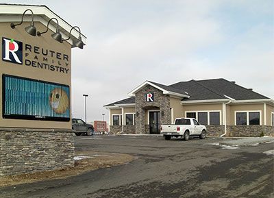 Reuter Family Dentistry office with sign, smiley face art, and parked vehicles.