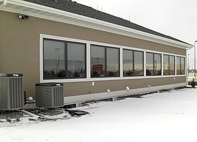 Exterior of a building with multiple windows, snow on the ground, two air conditioning units.