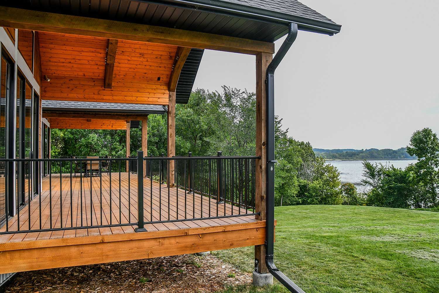 Wooden deck with black railing, overlooking a lake and trees.
