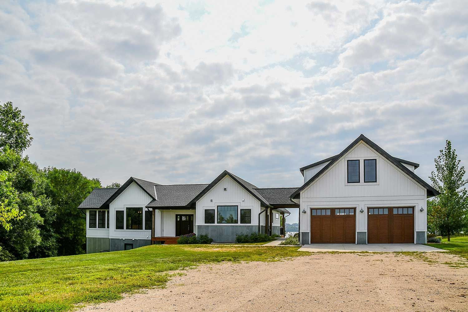 White farmhouse with brown garage doors on a grassy hill under cloudy sky.