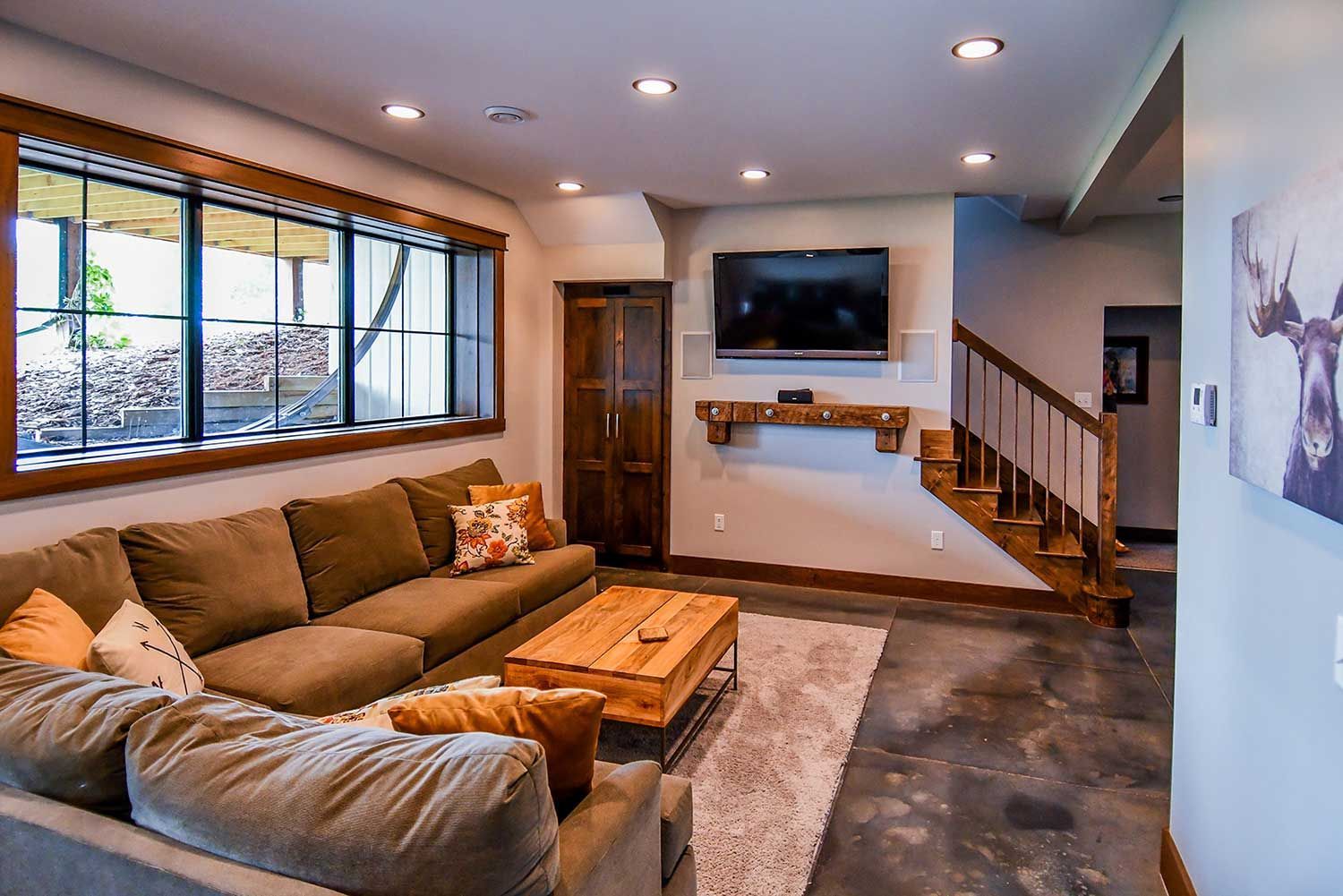 Cozy living room with a brown sectional sofa, wooden coffee table, TV, and a window overlooking a woodpile.