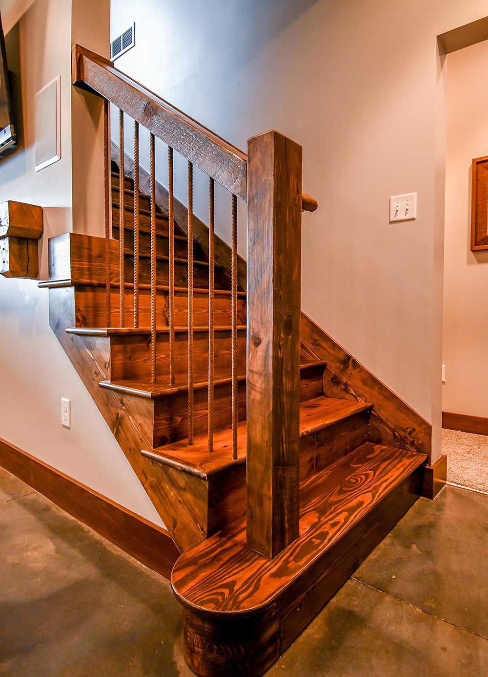Wooden staircase with metal railings; stained wood, neutral walls, and gray floor.
