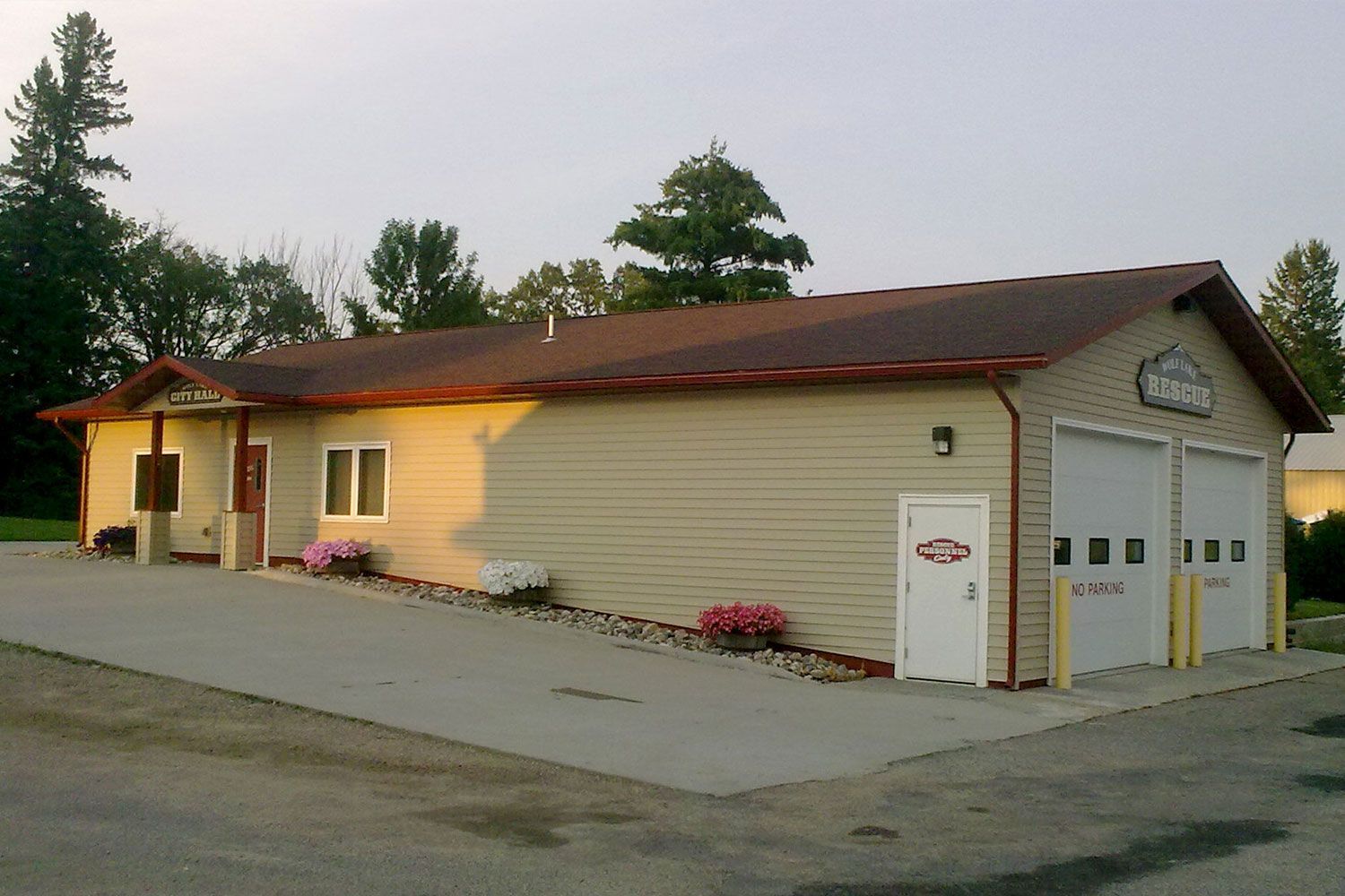 Tan building with two garage doors, a white door, and a red roof.