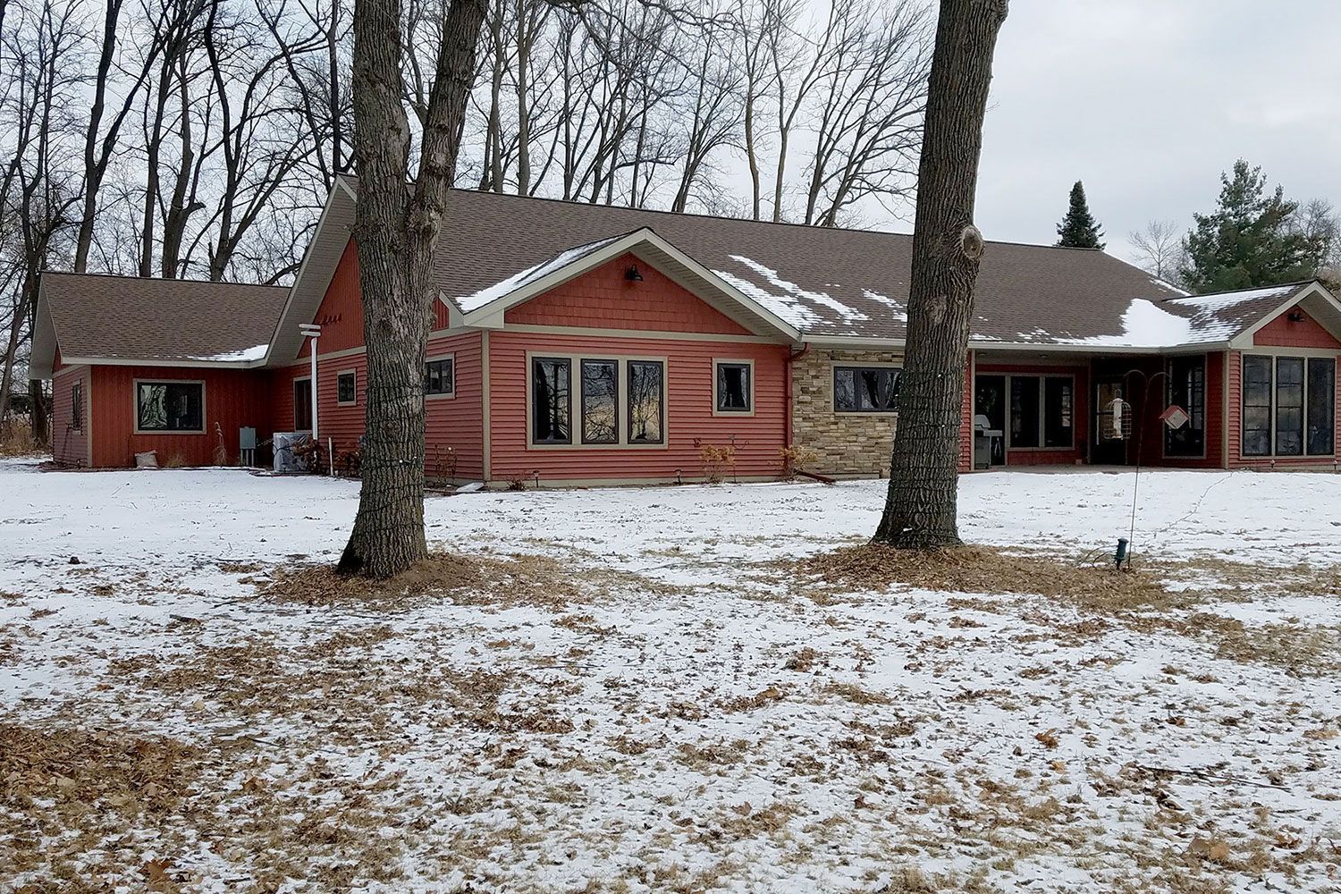 Red house with snow-covered yard and trees in winter; windows and brown roof are visible.
