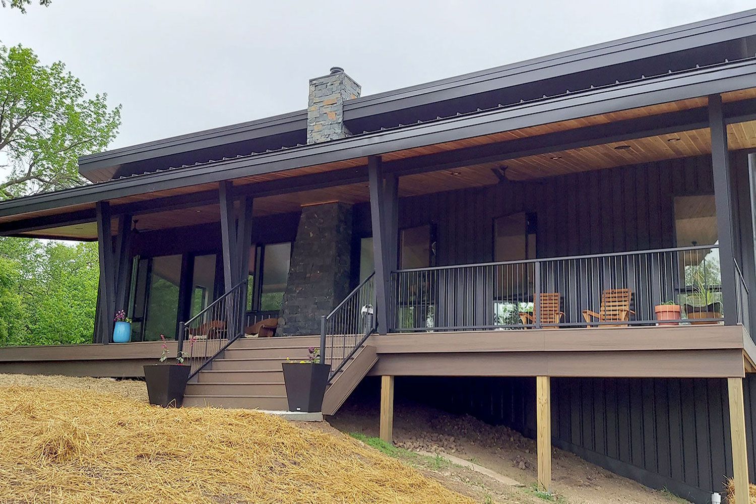 Brown and black cabin with a covered porch, stone chimney, and wooden steps leading up to the entrance.