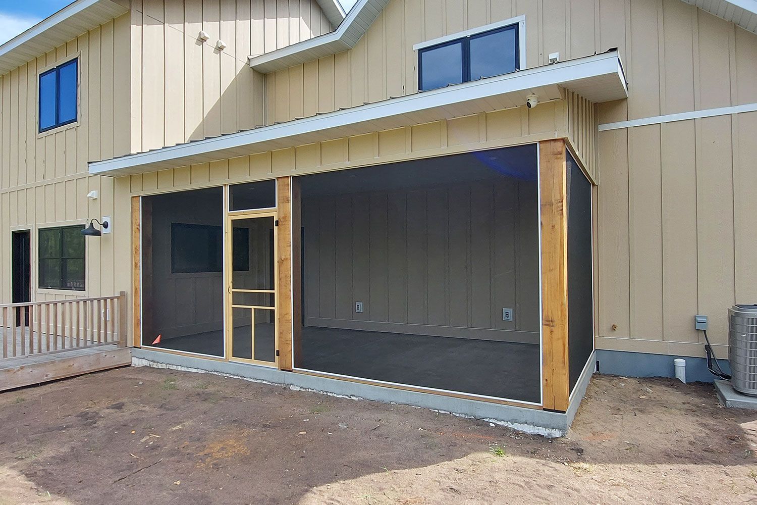 Screened-in porch extension on a beige house with wooden posts and a gray screen.