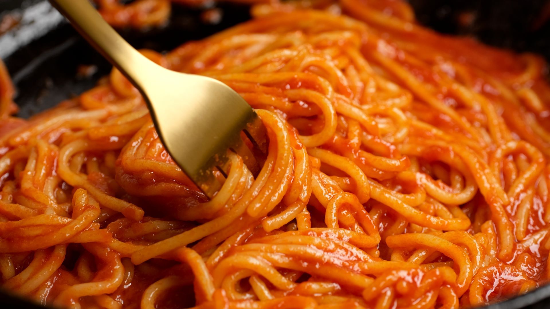 A close up of a pan of spaghetti with tomato sauce and a fork.