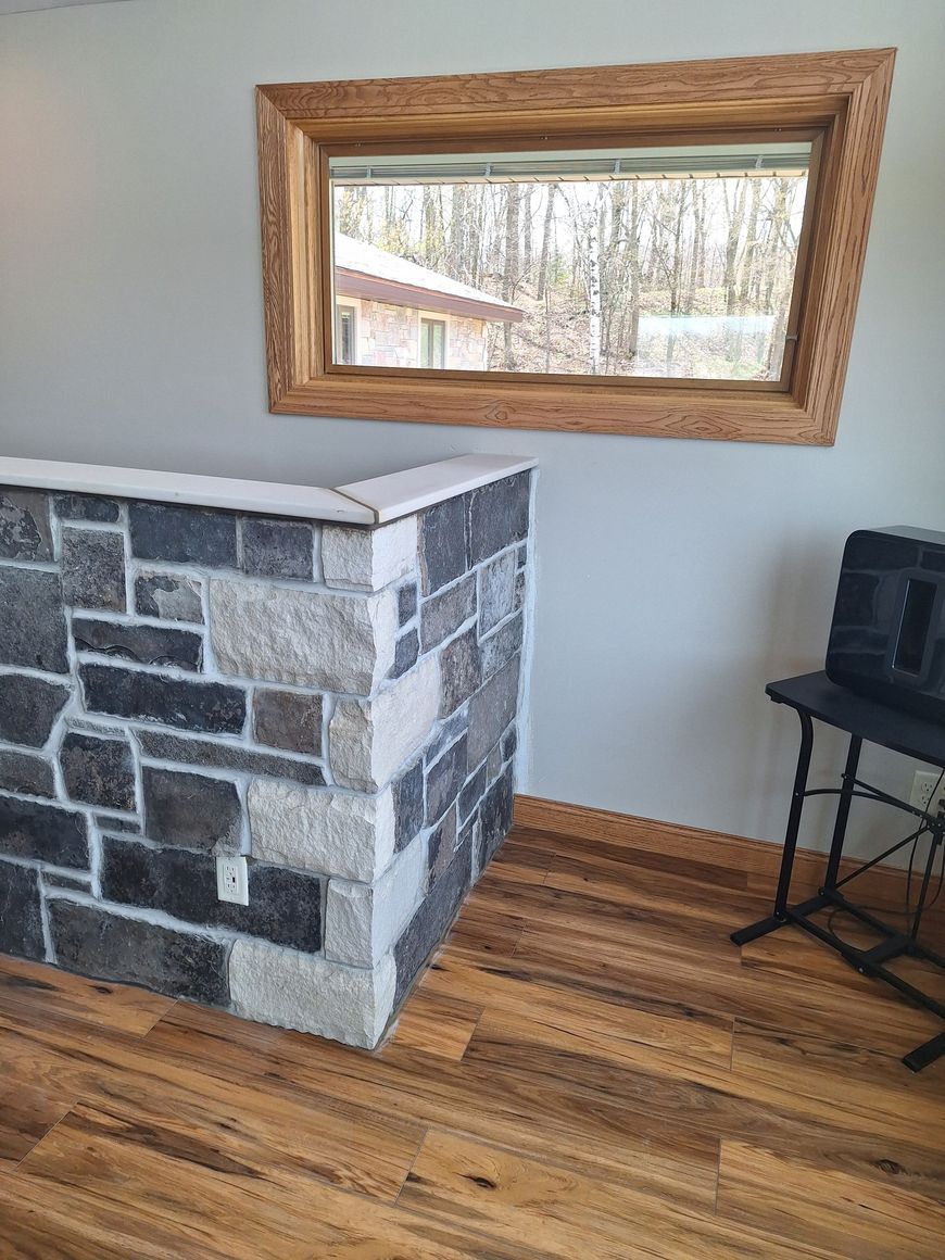 Stone-clad counter next to a window with a wooden frame and a piano bench on wood-look flooring.