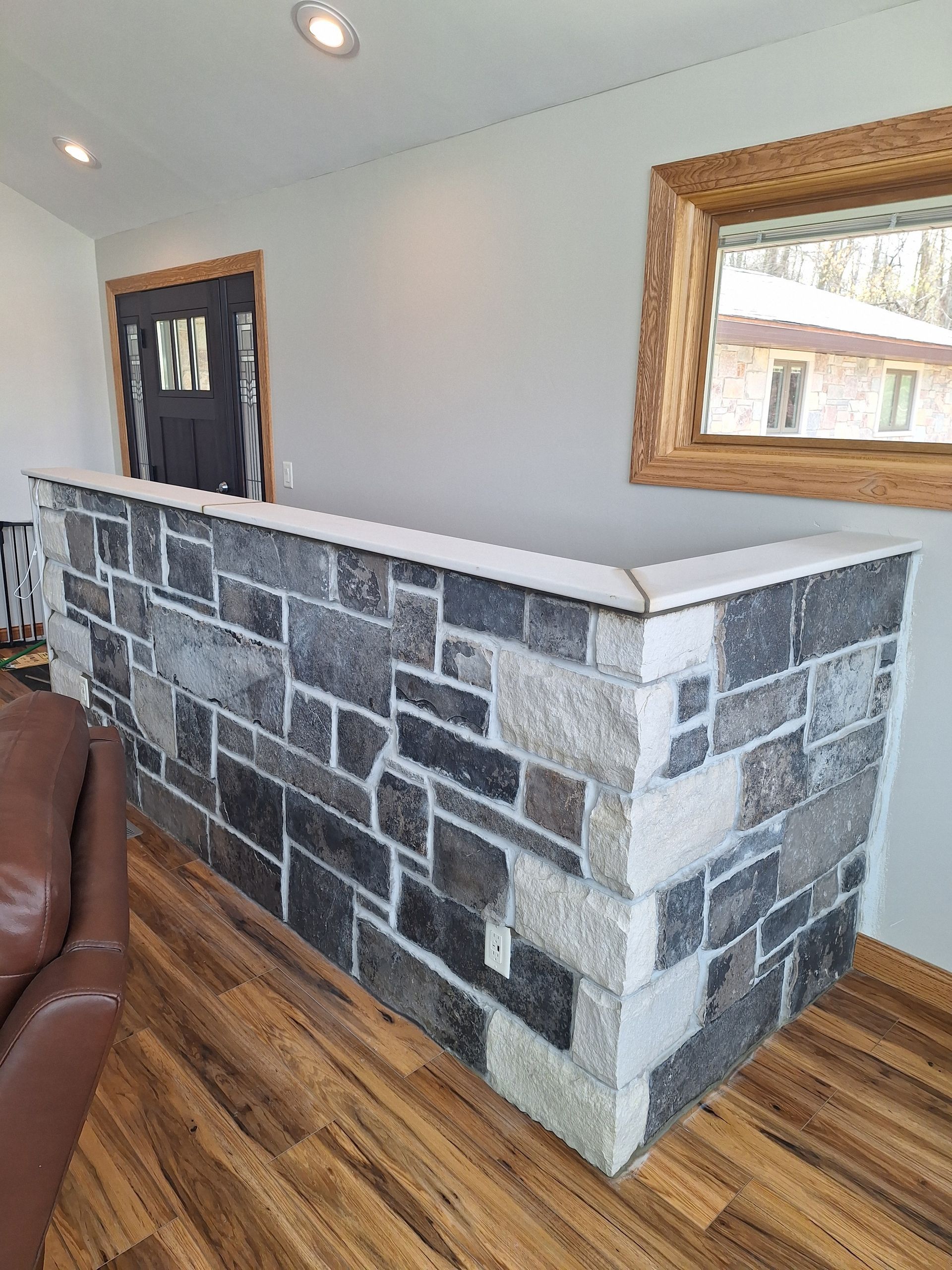 Stone-faced half-wall in a room with a countertop, wood flooring, and a door and window in the background.
