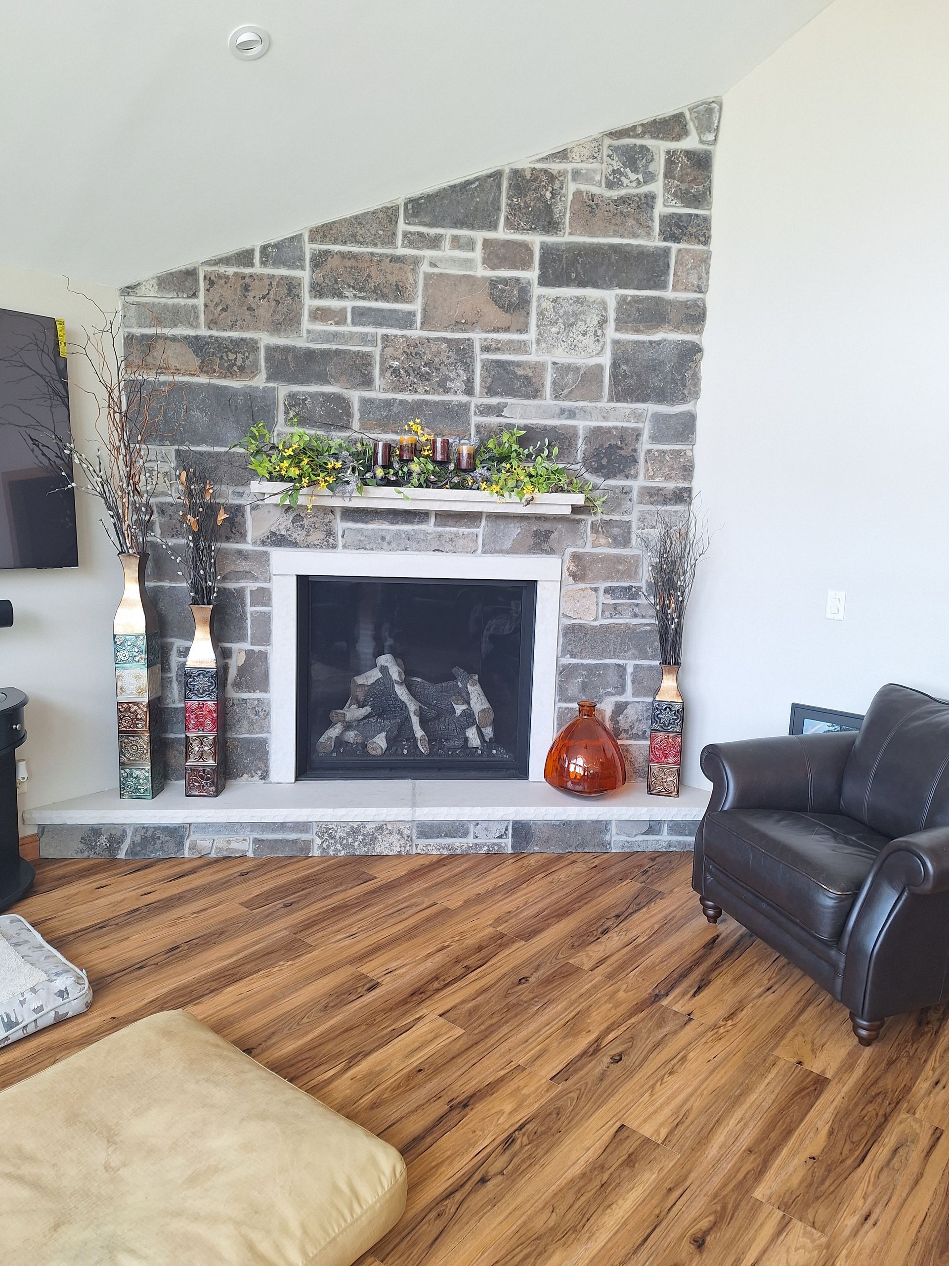 Fireplace with stone facade, white mantel, and brown leather armchair in a living room with wooden floors.