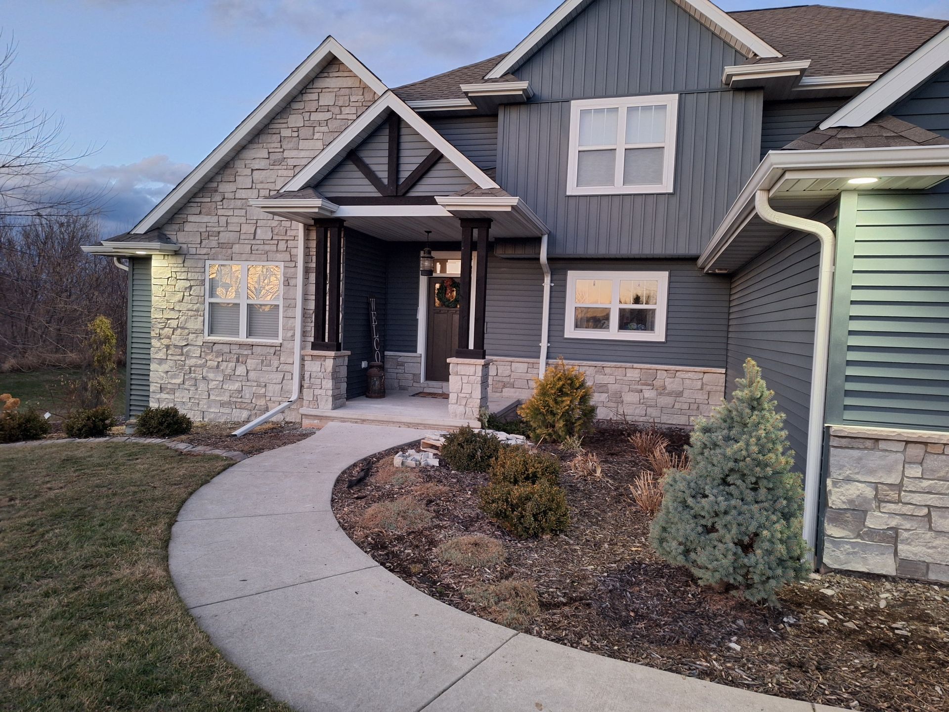 House with stone facade and blue siding, a walkway, and manicured landscaping.