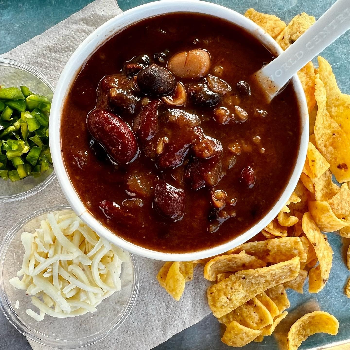 Hearty bowl of chili from The Soup Peddler, topped with shredded cheese and fresh herbs, served in a rustic bowl.