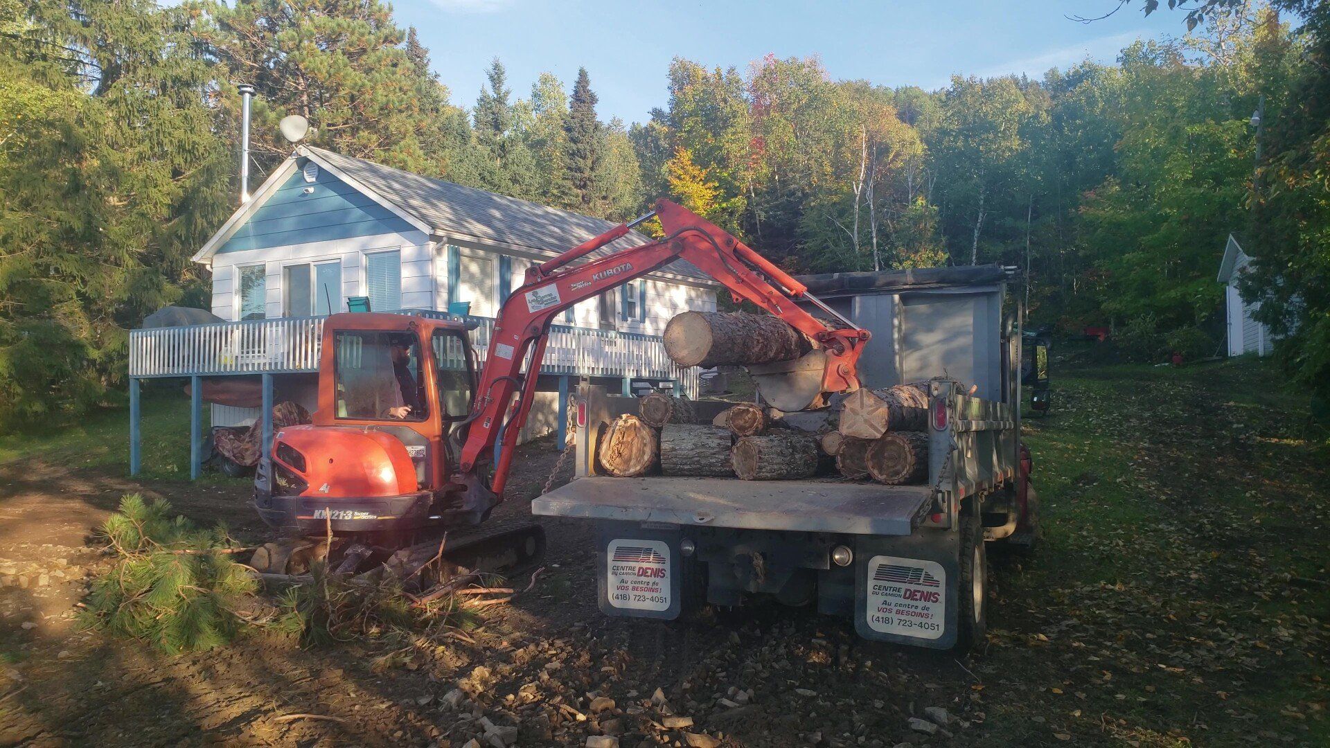 Un camion rempli de bûches est garé devant une maison.