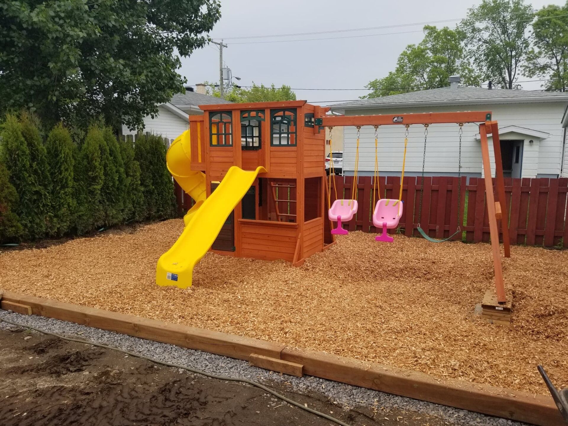 Une aire de jeux en bois avec un toboggan jaune et des balançoires dans une cour arrière.