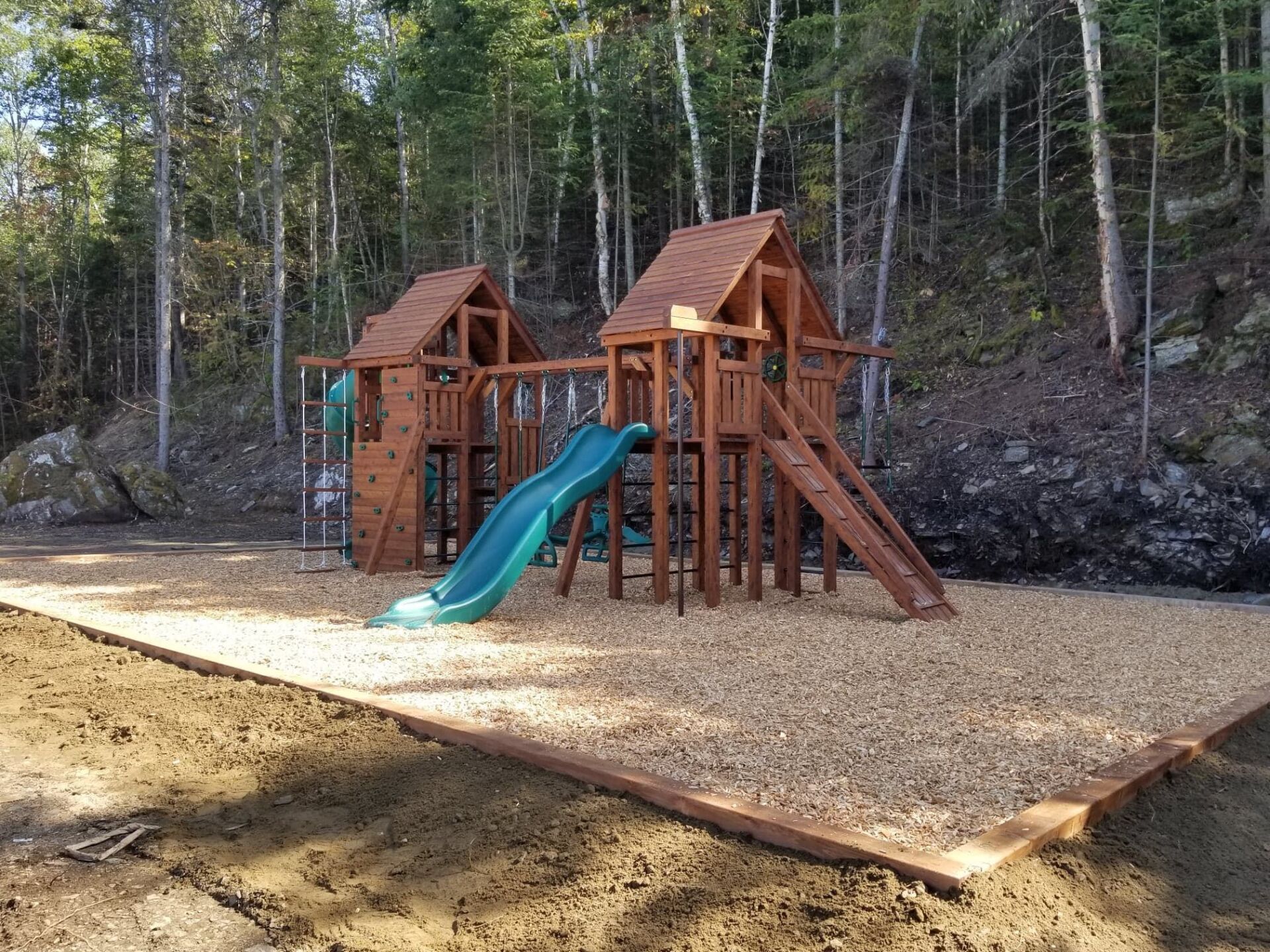 Une aire de jeux en bois avec un toboggan et des balançoires au milieu des bois.
