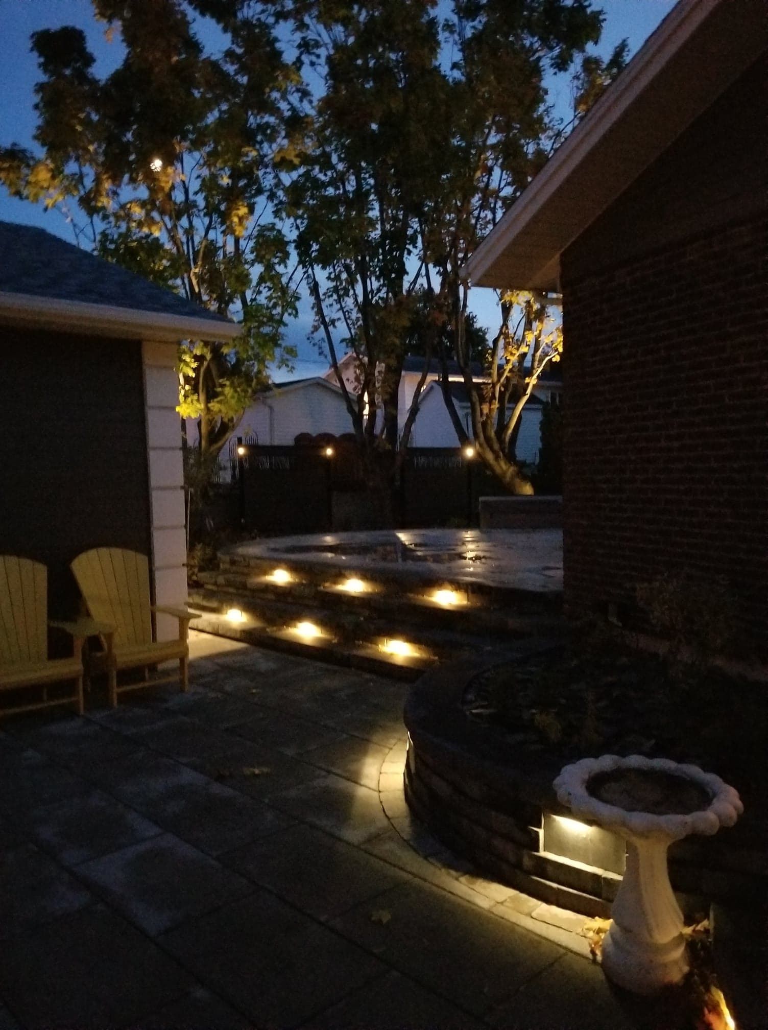 Une maison en briques avec un patio et des chaises éclairées la nuit