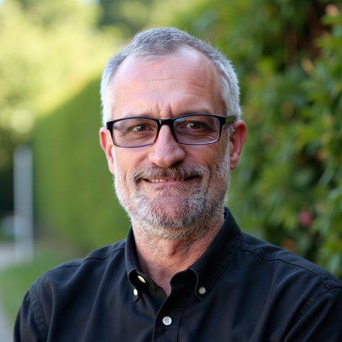 Woman with short, light-brown hair in a black polo shirt, looking at the camera. Office setting with blue walls and greenery.