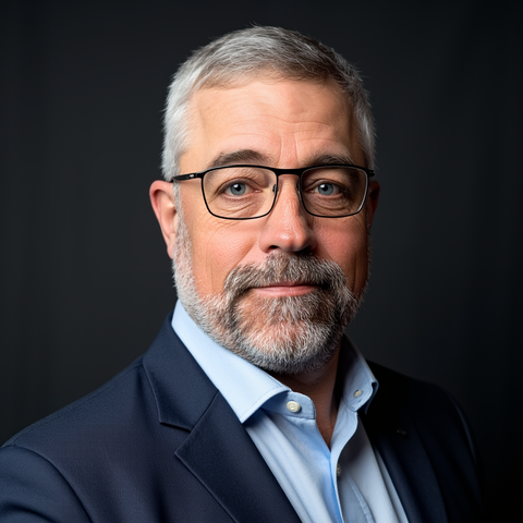 Man with glasses and red beard, wearing a suit in an office setting.